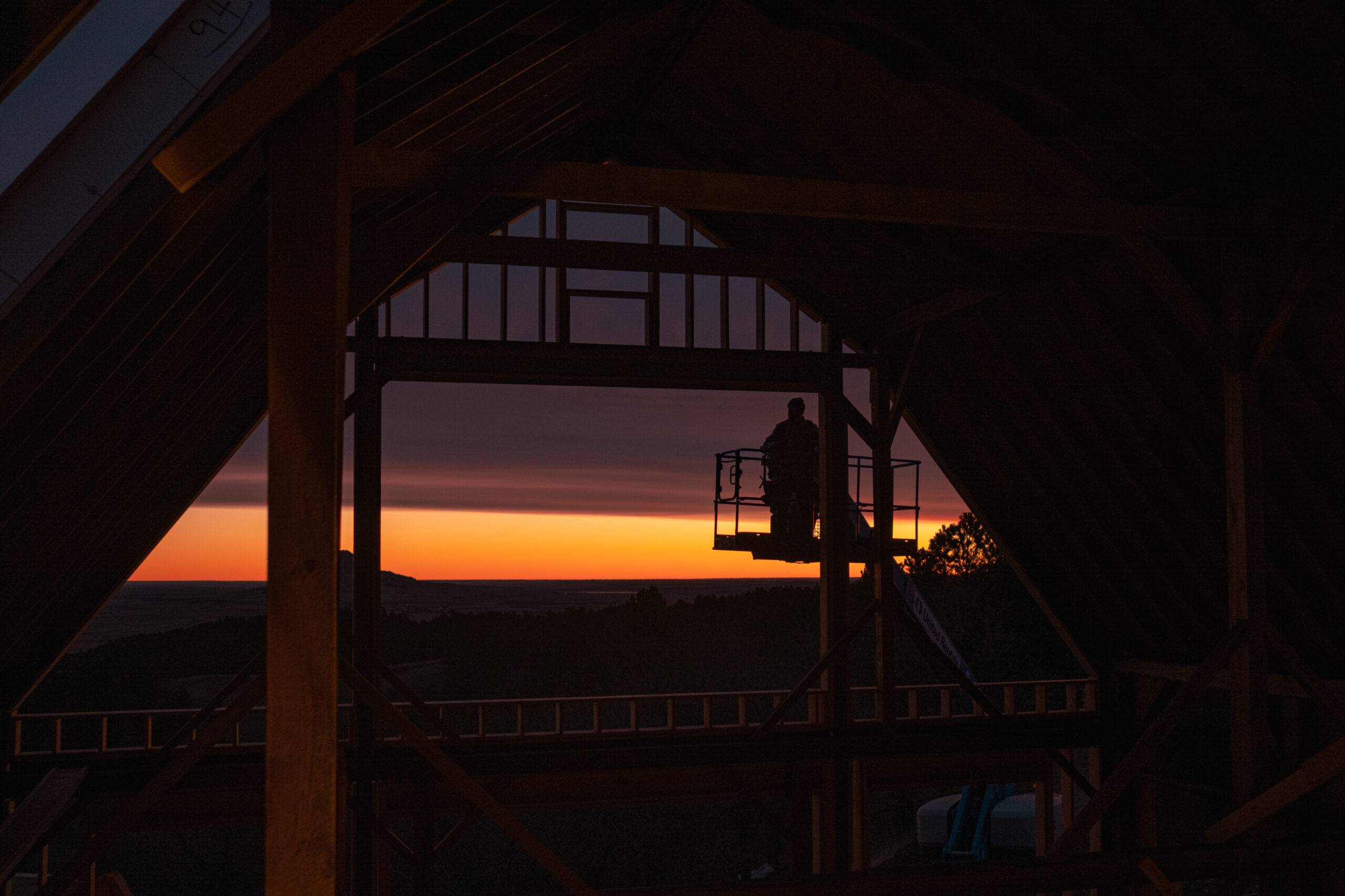 Timber frame builder working at sunrise to construct custom frame